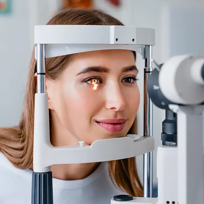 Woman undergoing refraction testing with advanced optical imaging equipment during comprehensive eye exam